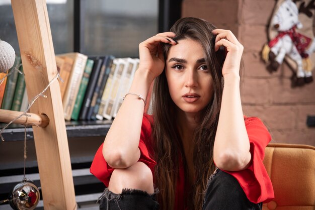 Un modelo de mujer joven en blusa roja sentada y posando.