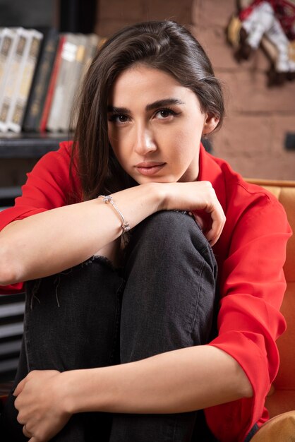 Un modelo de mujer joven en blusa roja sentada y posando.