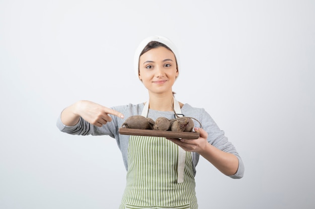 modelo de mujer joven y bonita en delantal apuntando a una tabla de madera con remolachas.