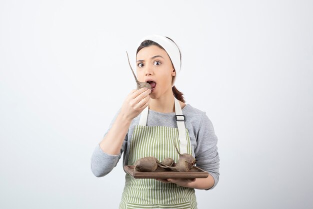 modelo de mujer joven y bonita en delantal comiendo una remolacha.