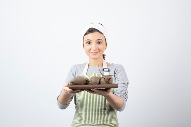 modelo de mujer joven y bonita en delantal sosteniendo una tabla de madera con remolachas.