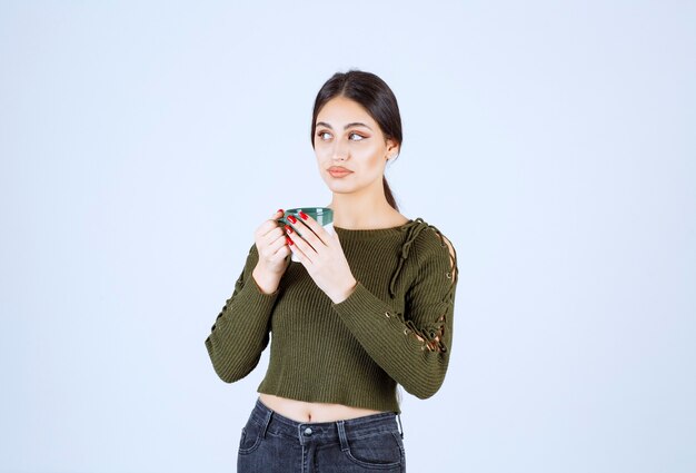 Un modelo de mujer joven y bonita sosteniendo una taza de bebida y mirando a otro lado.