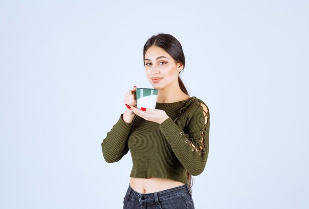 Un modelo de mujer joven y bonita sosteniendo una taza de bebida y de pie.