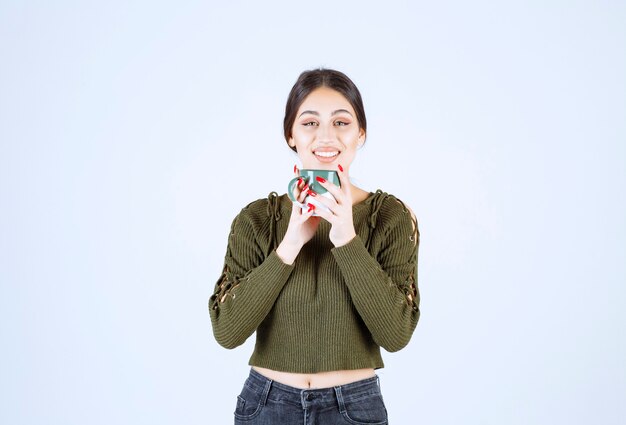 Un modelo de mujer joven y bonita sosteniendo una taza y mirando a la cámara