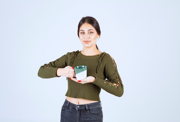 Un modelo de mujer joven y bonita sosteniendo una taza y mirando a la cámara