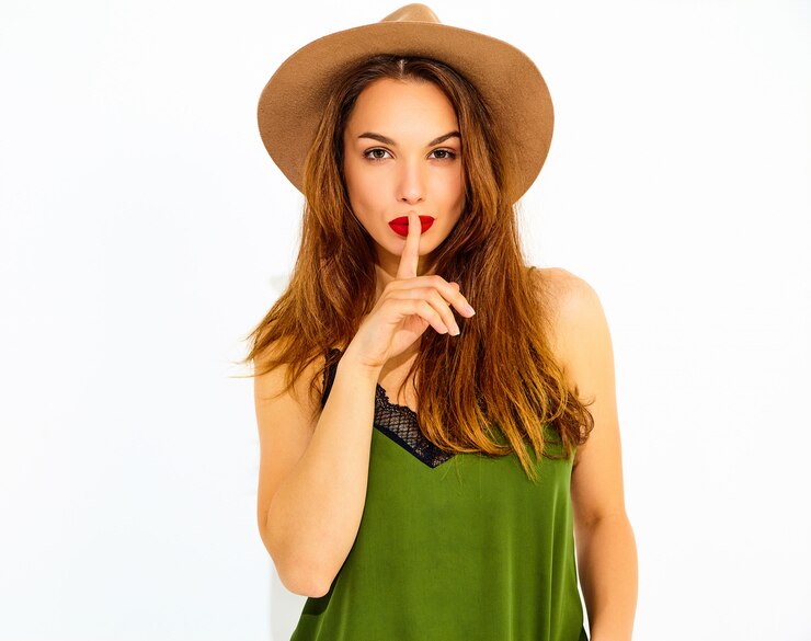 Foto gratuito modelo de mujer joven y elegante en ropa casual de verano verde y sombrero marrón con labios rojos mostrando gesto de silencio con el dedo, aislado