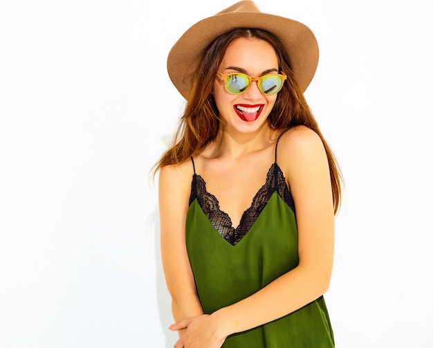 Modelo de mujer joven y elegante en ropa casual de verano verde y sombrero marrón con labios rojos, mostrando su lengua