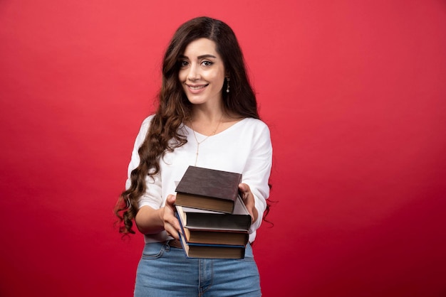 Modelo de mujer joven ofreciendo libros sobre un fondo rojo. Foto de alta calidad