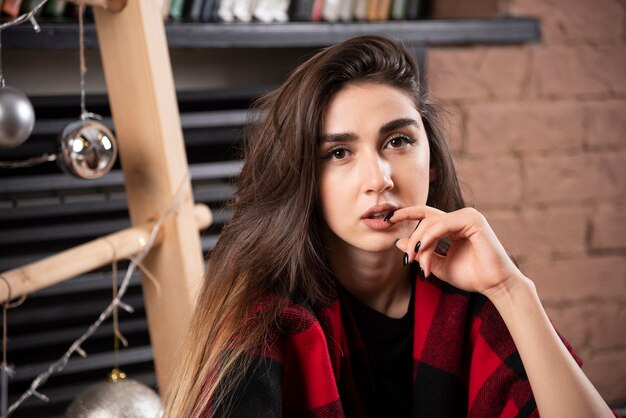 Modelo de mujer joven posando con cuadros escoceses cerca de bolas de Navidad.