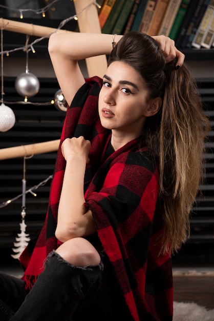Modelo de mujer joven posando con cuadros escoceses cerca de bolas de Navidad.