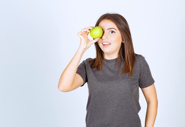 modelo de mujer joven que cubre su ojo con una manzana verde.