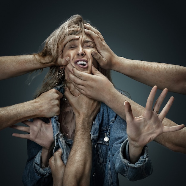 Un modelo de mujer joven rodeada de manos masculinas como sus propios pensamientos o problemas en la pared oscura