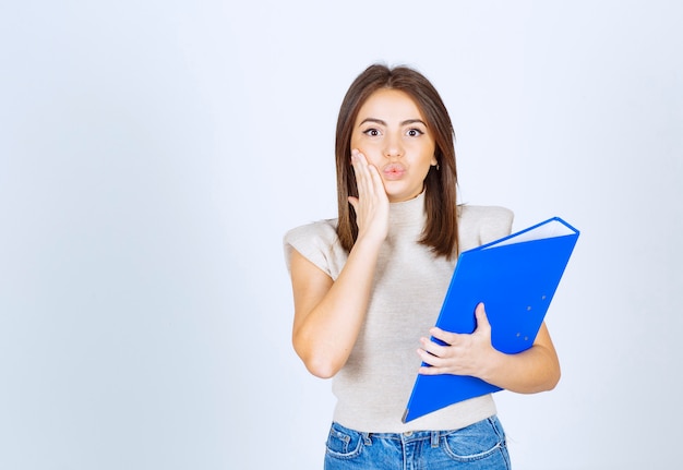 modelo de mujer joven sosteniendo una carpeta azul sobre una pared blanca.