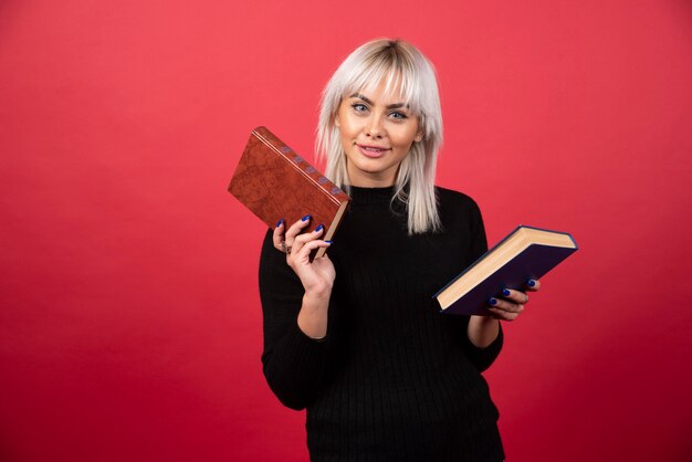 Modelo de mujer joven sosteniendo dos libros sobre un fondo rojo. Foto de alta calidad