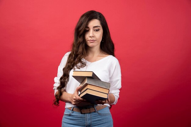 Modelo de mujer joven sosteniendo libros sobre un fondo rojo. Foto de alta calidad