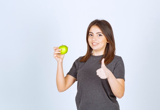 modelo de mujer joven sosteniendo una manzana verde y mostrando un pulgar hacia arriba.