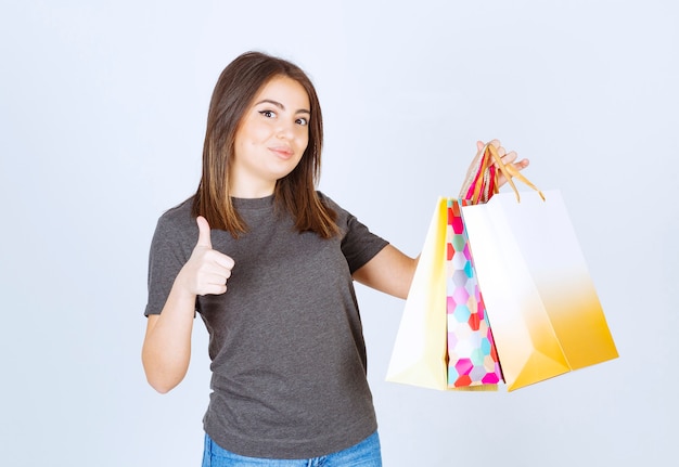 Un modelo de mujer joven sosteniendo un montón de bolsas de la compra y mostrando un pulgar hacia arriba.