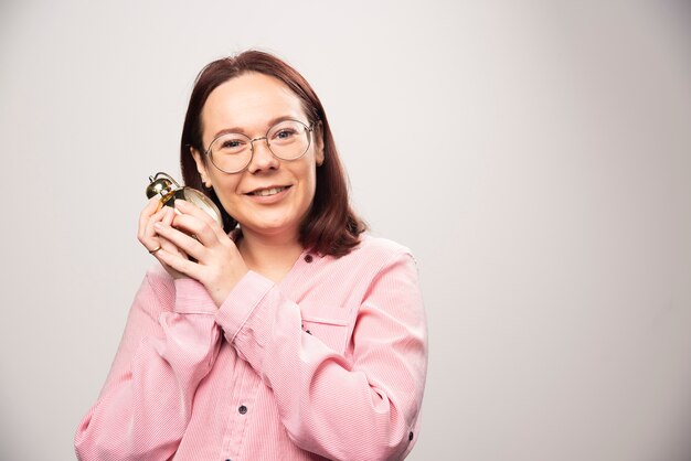 Modelo de mujer joven sosteniendo un reloj de alarma sobre un fondo blanco. Foto de alta calidad