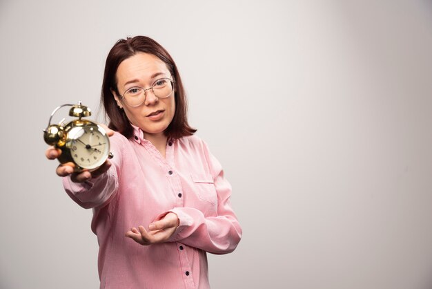 Modelo de mujer joven sosteniendo un reloj de alarma sobre un fondo blanco. Foto de alta calidad