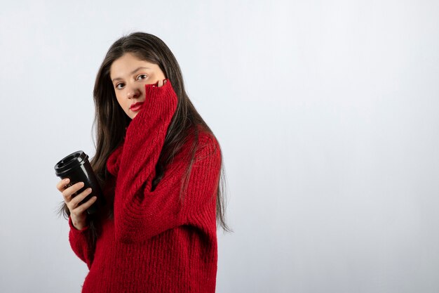 Un modelo de mujer joven en suéter rojo sosteniendo una taza de café