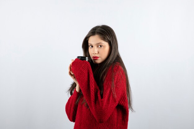 Un modelo de mujer joven en suéter rojo sosteniendo una taza de café