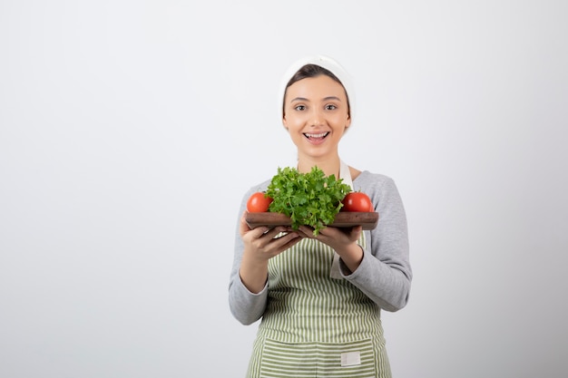 modelo de mujer linda sonriente sosteniendo una tabla de madera con verduras frescas.