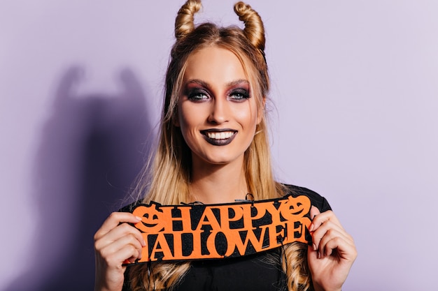 Foto gratuita modelo de mujer riendo con maquillaje de halloween oscuro posando en la pared púrpura. foto interior de una chica bastante rubia.