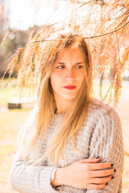 Modelo de mujer rubia mirando a un lado debajo de la corona de árbol