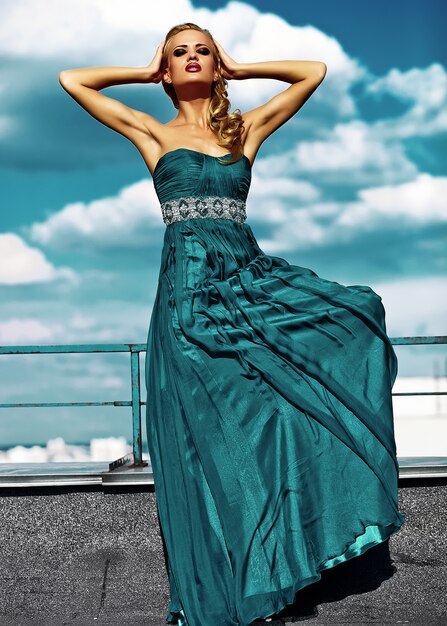 Modelo de mujer rubia sexy joven en traje de noche posando sobre fondo de cielo azul