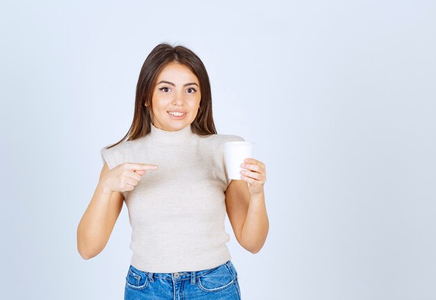 Un modelo de mujer sonriente apuntando a un vaso de plástico y posando.