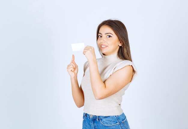 Un modelo de mujer sonriente de pie y apuntando a una tarjeta sobre fondo blanco.