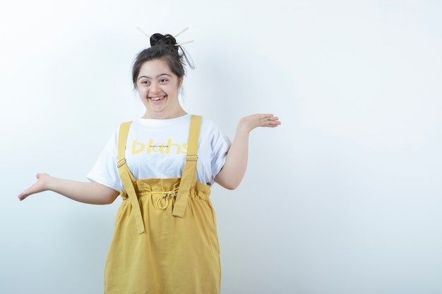 Modelo de niña bonita de pie y sonriendo contra la pared blanca.