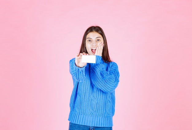 modelo de niña sonriente mostrando una tarjeta en la pared rosa.