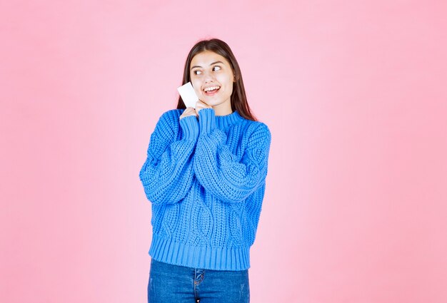 modelo de niña sonriente sosteniendo una tarjeta en la pared rosa.