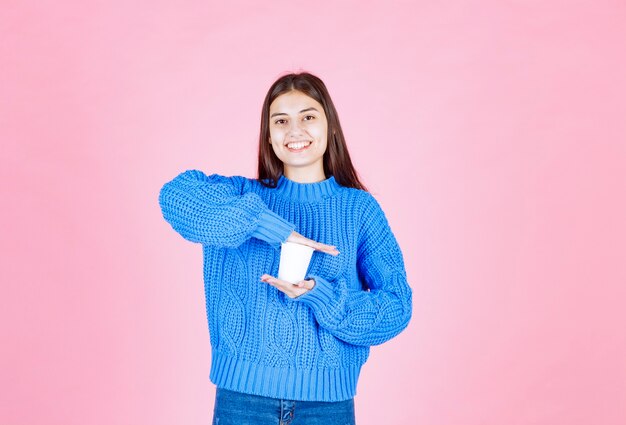 modelo de niña sosteniendo un vaso de plástico en la pared rosa.