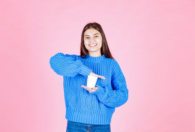 modelo de niña sosteniendo un vaso de plástico en la pared rosa.