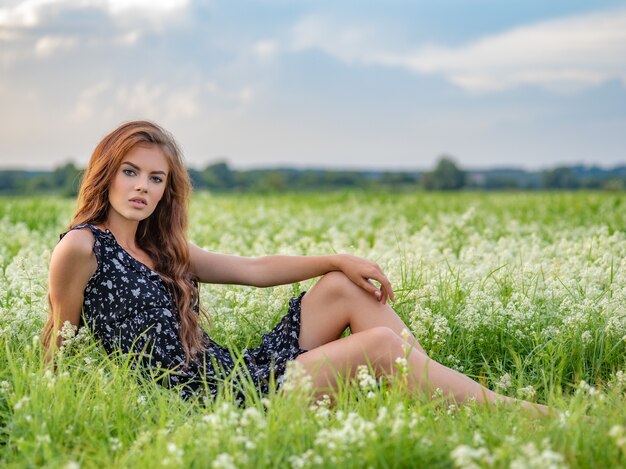 Modelo posando en un campo de flores blancas de lavanda. Mujer joven sentada al aire libre en un campo de flores blancas.