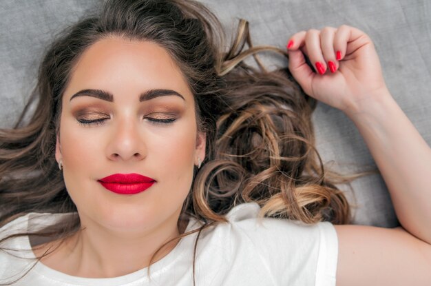 Modelo sensual de la mujer con el pelo azotado por el viento pelo moreno sobre fondo gris claro. Peinado largo brillante de la salud. Belleza y cuidado del cabello. Maquillaje natural de la manera