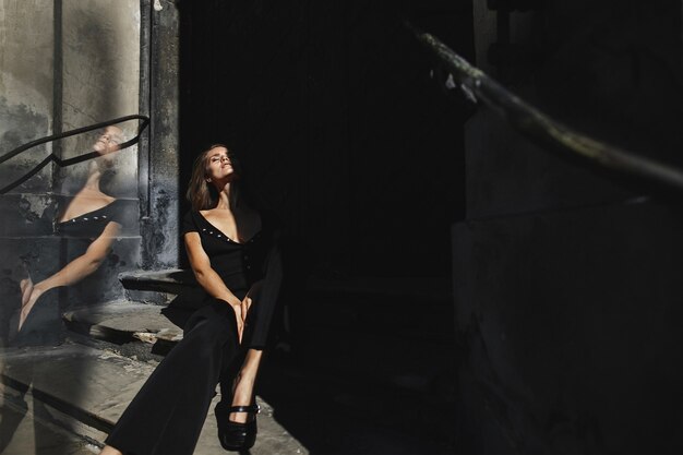 Modelo vestida con el traje negro se sienta en las escaleras del antiguo edificio