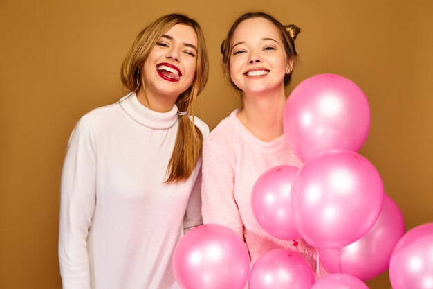 Modelos de mujeres con globos rosados en la pared dorada