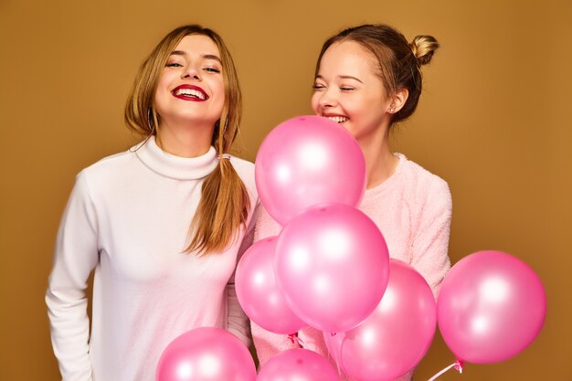 Modelos de mujeres con globos rosados en la pared dorada