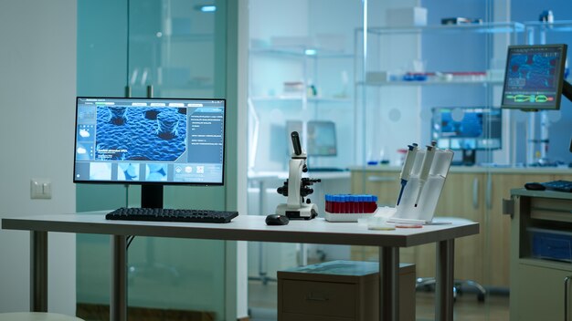 Moderno laboratorio de ciencias biológicas aplicadas vacío con microscopios tecnológicos, tubos de ensayo de vidrio, micropipetas, computadoras de escritorio y pantallas. Las PC están ejecutando sofisticados cálculos de ADN.