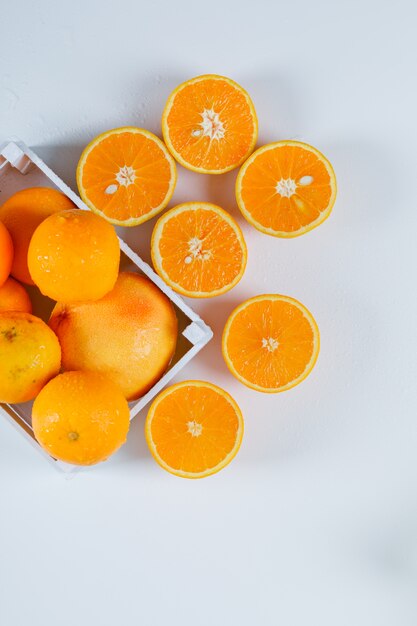 Moje las naranjas con mitades en un recipiente rectangular blanco sobre una superficie blanca, plano.