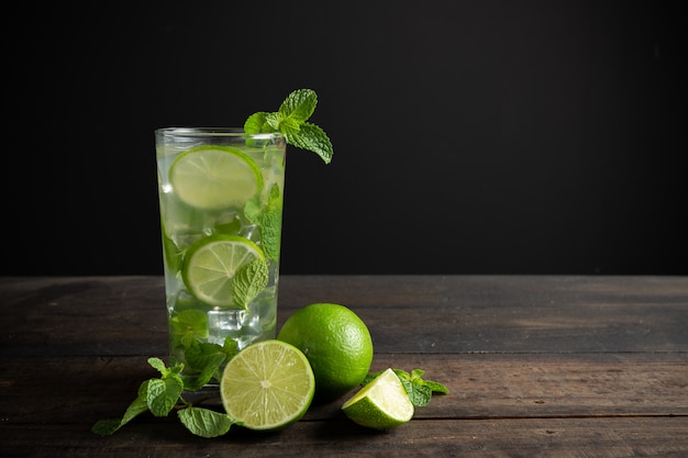 Mojito de bebida con lima, limón y menta en mesa de madera.