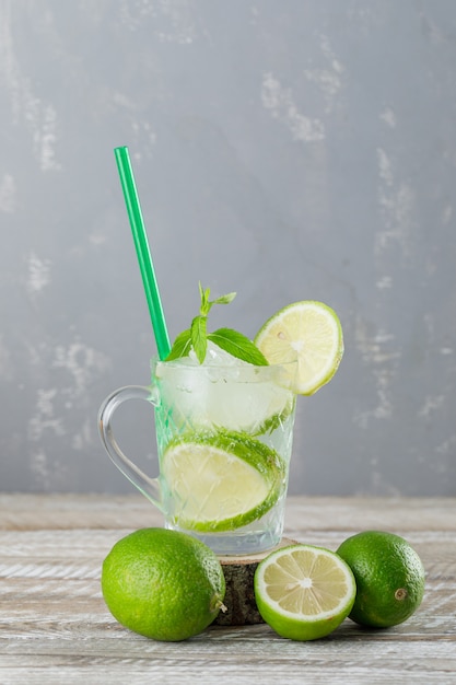 Foto gratuita mojito helado cóctel en una taza con limas, menta, paja vista lateral en madera y pared de yeso