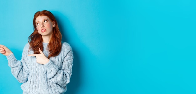 Foto gratuita molesta adolescente pelirroja pone los ojos en blanco apuntando con el dedo a la izquierda en algo aburrido o cojo de pie ir