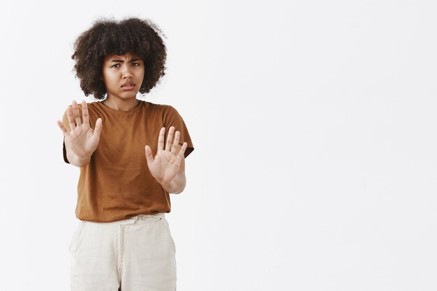 Molesta intensa dispelased joven afroamericana con cabello rizado tirando de las manos hacia en gesto de protección dando rechazo o rechazo