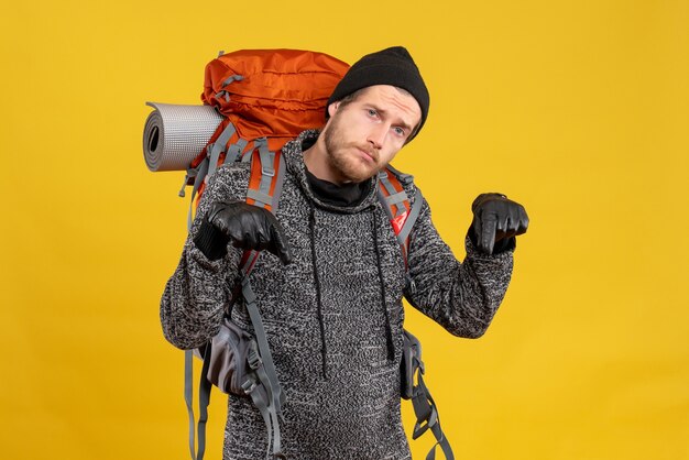 Molesto autoestopista masculino con guantes de cuero y mochila apuntando al piso