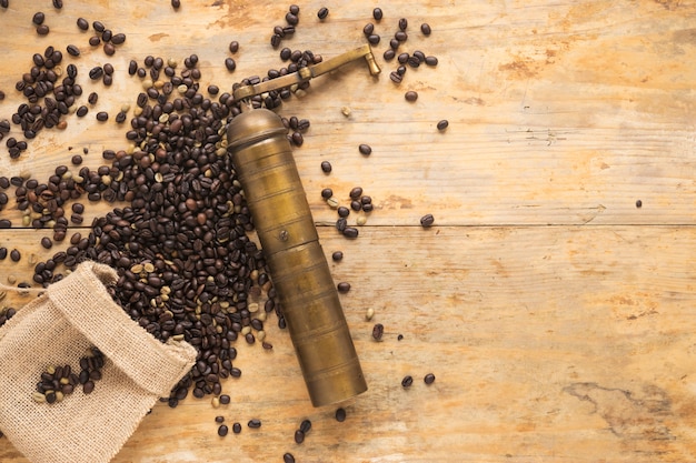 Molinillo de café viejo con los granos de café que caen del saco en la tabla