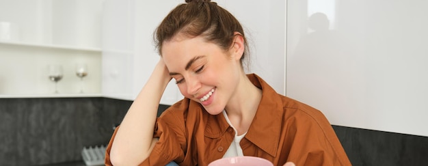 Foto gratuita momentos acogedores feliz joven se sienta en la cocina y bebe café tiene una sonrisa tierna en su rostro